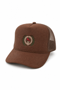 Load image into Gallery viewer, A brown trucker hat with a suede-like front panel and mesh back, featuring a circular embroidered logo on the front with a red cardinal and green laurel wreath.